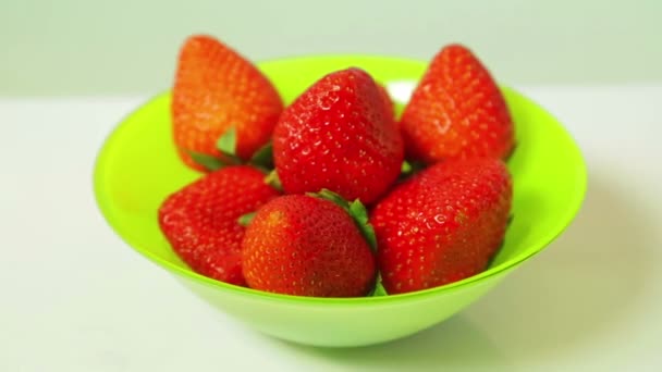 Rote frische Erdbeeren in einem grünen Teller auf blauem Hintergrund drehen sich im Kreis — Stockvideo