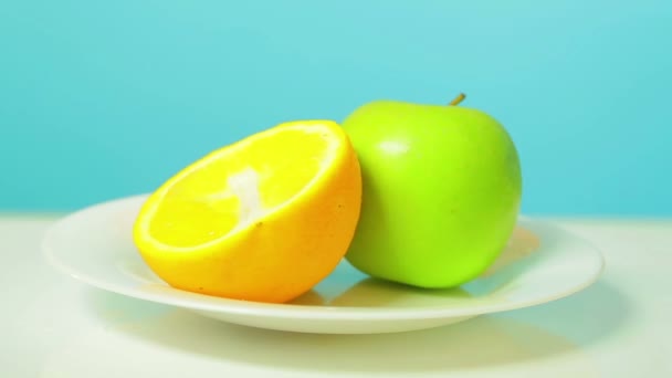 A metade de maçã verde inteira de quivi e laranja em uma chapa branca gira em um círculo — Vídeo de Stock