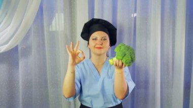 Bir kadın bir önlük gülümsüyor yemek, elinde brokoli tutar ve elini Ok gösterir