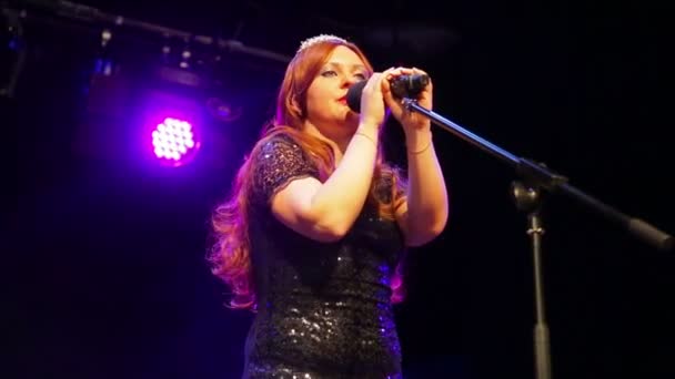 Una joven actriz con un vestido negro brillante está cantando en el escenario en el micrófono en una bocanada de humo — Vídeos de Stock