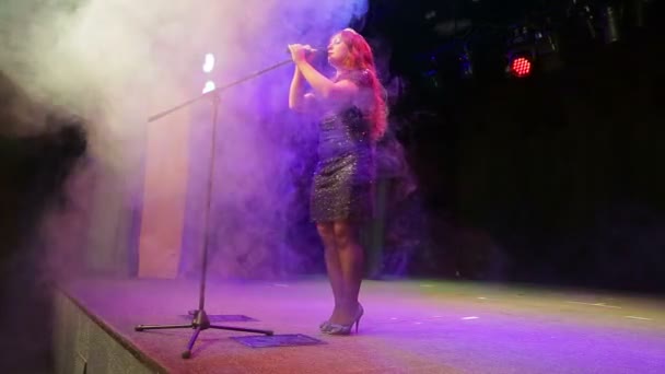 Young redhead female singer in full growth on the stage at the microphone in a puff of smoke — 비디오