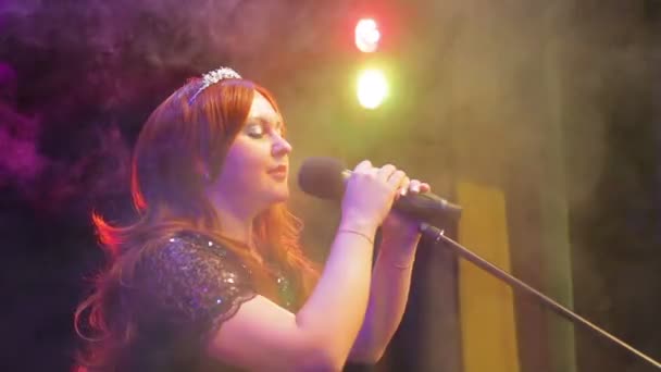 Joven cantante pelirroja cantando en el escenario en el micrófono en una bocanada de humo . — Vídeo de stock