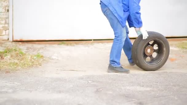 Un hombre mecánico automático rueda sobre un neumático de asfalto con un disco — Vídeos de Stock