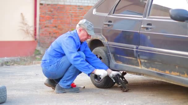 Un mecánico automático macho baja el coche al suelo y fija la rueda en el eje del coche. Vueltas de tiempo . — Vídeo de stock