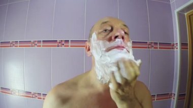 Banyodaki adam yüzüne tıraş köpüğü koyuyor.