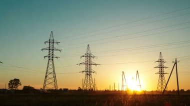 Yolun yanındaki kırsal alanda gün batımı ve yüksek voltajlı elektrik hatları arasında geçen arabalar. Zaman atlamalı. Genel plan