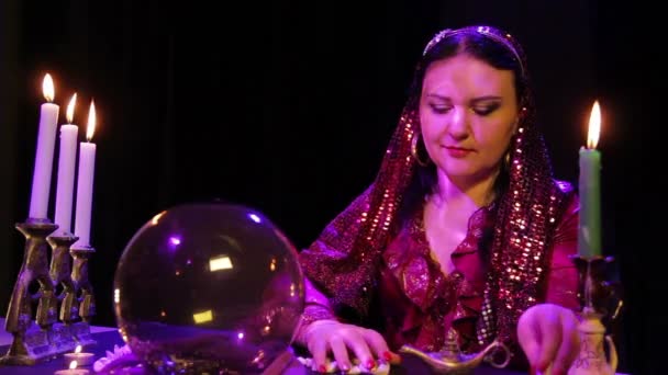 Zigeunerin im roten Kleid im Rauch bei Kerzenschein liest die Zukunft in den Steinen — Stockvideo