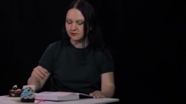 Kafede bir kadın siyah bir arka plan üzerinde beyaz bir fincan kahve içiyor ve bir günlük yazıyor
