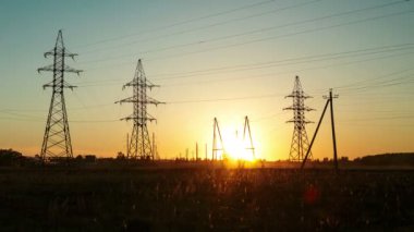 Yüksek voltajlı elektrik hatlarının arka planına karşı kırsal kesimde gün batımı. Zaman turları