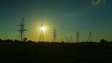 Gün batımında kırsal kesimdeki yüksek voltajlı elektrik hatlarının arka planına karşı bulutları çalıştırıyor. Zaman turları