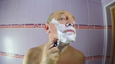 Banyodaki bir adam, tapınaklarının etrafındaki sakalı jiletle tıraş ediyor..