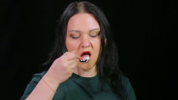 Een brunette vrouw op een zwarte achtergrond is het drinken van koffie en het eten van een cake — Stockvideo