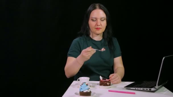 Una mujer morena sobre un fondo negro en un café está bebiendo café y comiendo un pastel — Vídeo de stock