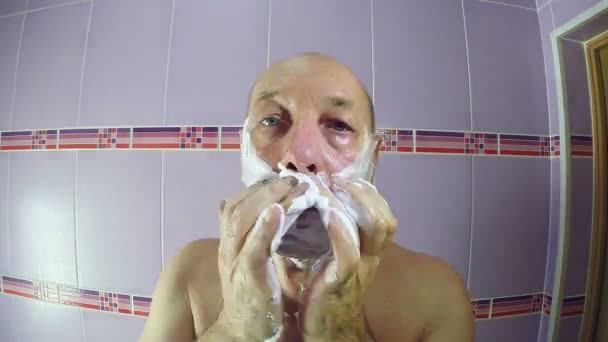 A férfi a fürdőszobában leborotválja arcát egy borotvát és darabos törülközőt. Időkörök — Stock videók