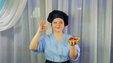 Önlüklü kadın gülümsüyor, elinde yeşil salata tutuyor ve elini gösteriyor.