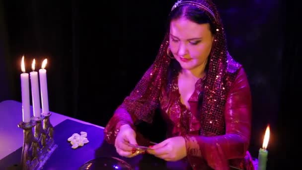 Циганка в червоній сукні в чарівному салоні свічками читає майбутнє на картах — стокове відео
