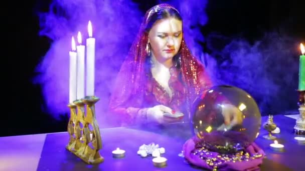 Gypsy in een rode jurk in een sjaal legt de kaarten in de reflecties van de kaarsen — Stockvideo