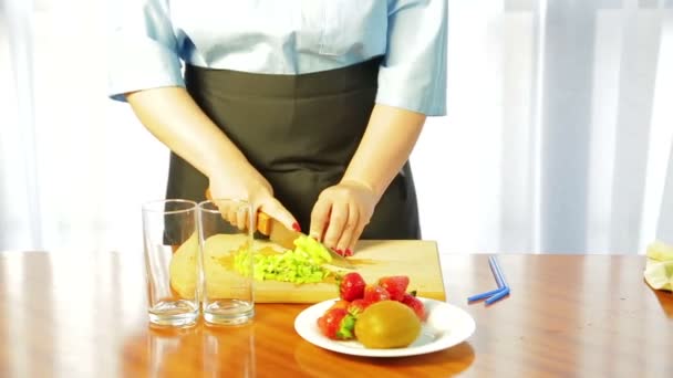 Woman slices ripe kiwi with a knife on a wooden board on slices — Αρχείο Βίντεο