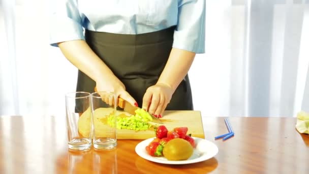 Woman slices ripe kiwi with a knife on a wooden board on slices — ストック動画