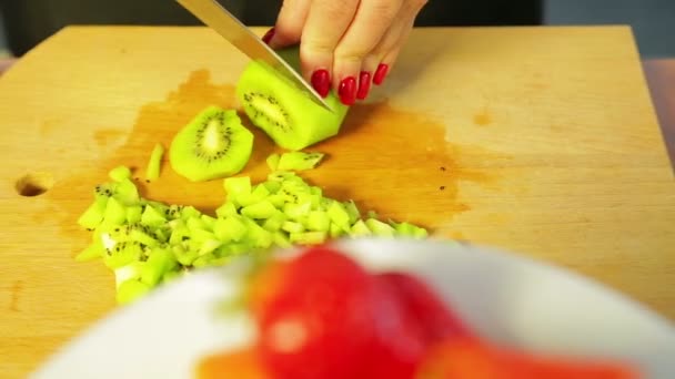 Woman cuts ripe kiwi with a knife on a wooden board — Stock Video