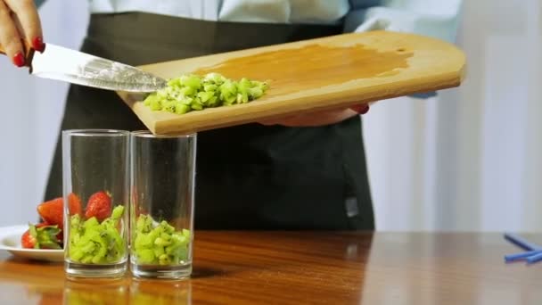 Eine Frau legt ein Stück Kiwi in ein Cocktailglas — Stockvideo