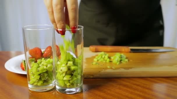 Женщина кладет кусок киви в бокал для коктейлей — стоковое видео