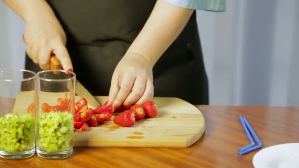 Une femme coupe des fraises mûres avec un grand couteau sur une planche de bois avec un grand couteau — Video