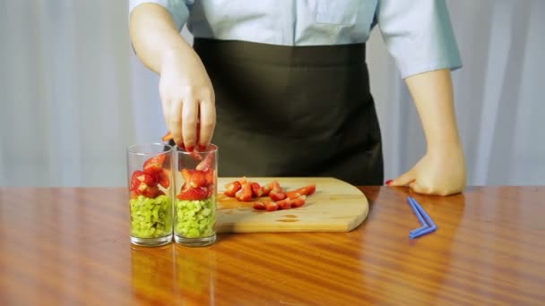 Une femme met dans un verre avec des tranches de kiwi écrasées et des fraises mûres — Video