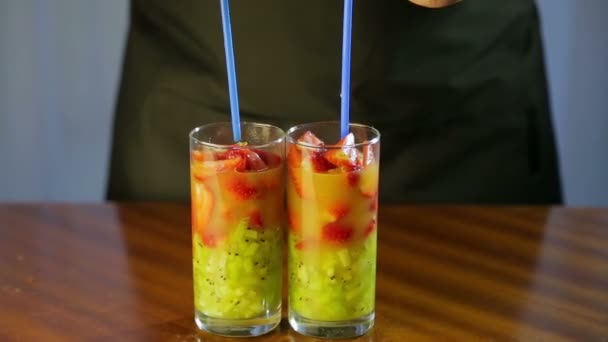 Donna inserisce tubuli in bicchieri con un cocktail di kiwi e fragole — Video Stock