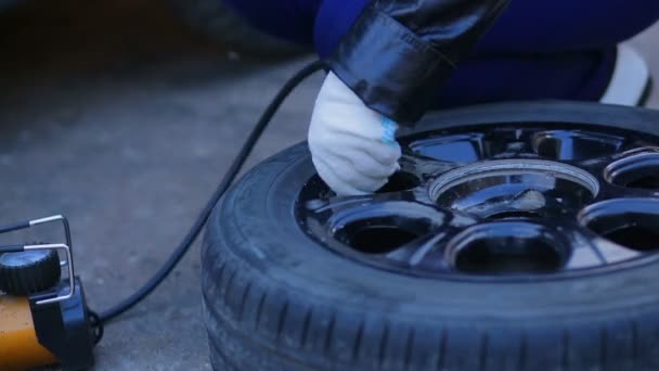 Uma mulher de luvas está bombeando um pneu de carro com um compressor . — Vídeo de Stock