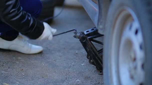 Frau mit Handschuhen hebt Auto mit Wagenheber an. — Stockvideo