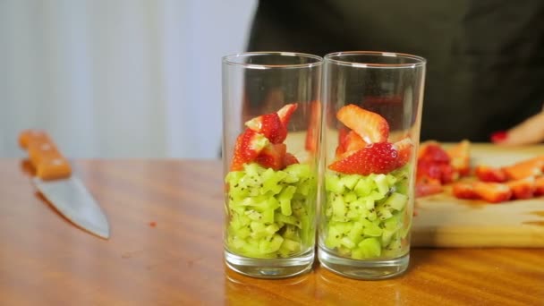 Eine Frau gibt ein Glas mit zerdrückten Kiwi-Scheiben und reifen Erdbeeren — Stockvideo
