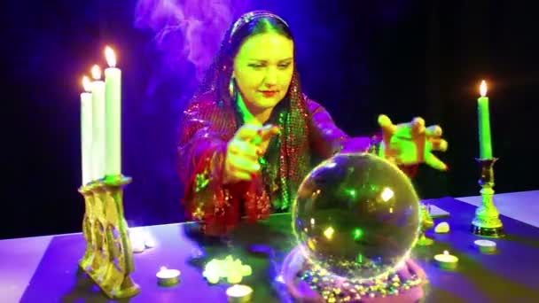 A gypsy in the magic salon is engaged in magic with a crystal ball, from which the Bitcoin fire sign appears — Stock Video