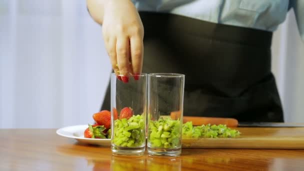 Une femme met un morceau de kiwi dans un verre à cocktail . — Video