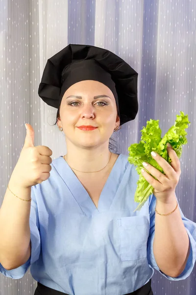 Positive female cook holding fresh green salad in her hands.