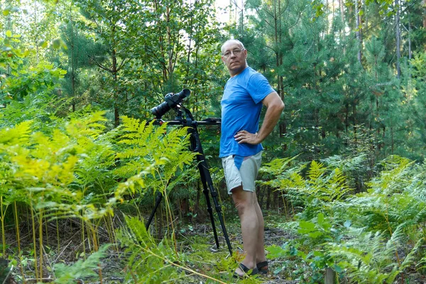 Tripod üzerinde kamera olan bir adam fotoğrafçı ormanda çekim yapan.