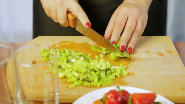 Woman slices ripe kiwi with a knife on a wooden board on slices — Αρχείο Βίντεο