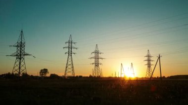 Yüksek voltajlı elektrik hatlarının arka planına karşı kırsal kesimde gün batımı. Zaman turları