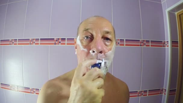 De man in de badkamer scheert de stoppel van zijn wangen en kin met een scheermes — Stockvideo