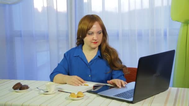 A brown-haired woman in a cafe at a table works with a laptop and drinks coffee — Stock Video