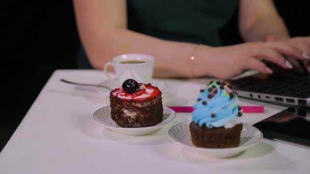 Pasteles en la mesa en el café detrás del cual las manos de las mujeres están escribiendo en el ordenador — Vídeos de Stock