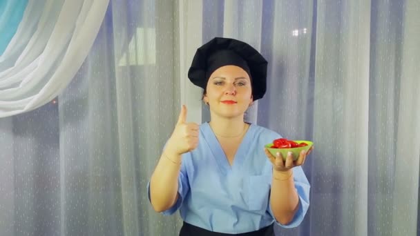 Donna cuoco in grembiule sorride, tiene in mano pomodorini ciliegini in un piatto e mostra classe con la mano — Video Stock