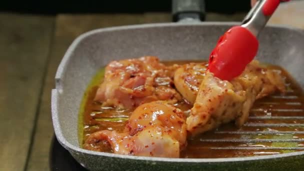 A womans hand turns the chicken over with a tongs on the grill pan and pours the sauce over it. — Stock Video