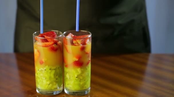 Mujer inserta túbulos en vasos con un cóctel de kiwi y fresas — Vídeos de Stock