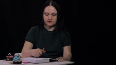 Kafede bir kadın siyah bir arka plan üzerinde beyaz bir fincan kahve içiyor ve bir günlük yazıyor.