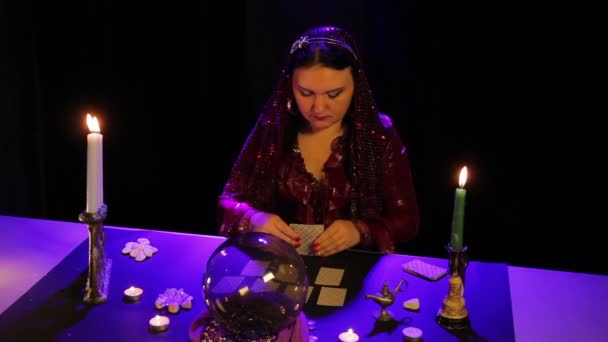 V kouzelném salonu si cikánka rozloží karty na černém stole v záři. — Stock video