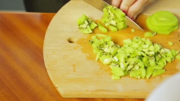 Femme coupe kiwi mûr avec un couteau sur un cube de planche en bois — Video