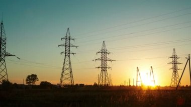 Yolun yanındaki kırsal alanda gün batımı ve yüksek voltajlı elektrik hatları arasında geçen arabalar. Zaman turları