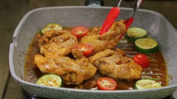 Ręka womans zamienia kawałki warzyw z kleszcze i kurczaka na patelni grill i wylewa sos nad nim — Wideo stockowe