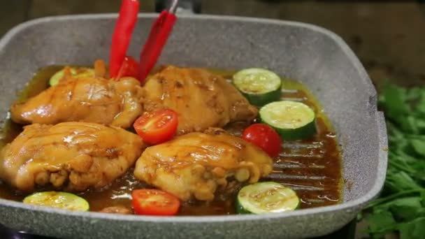 A womans hand turns the pieces of vegetables with forceps and chicken onto a grill pan and pours sauce over it. — Stock Video